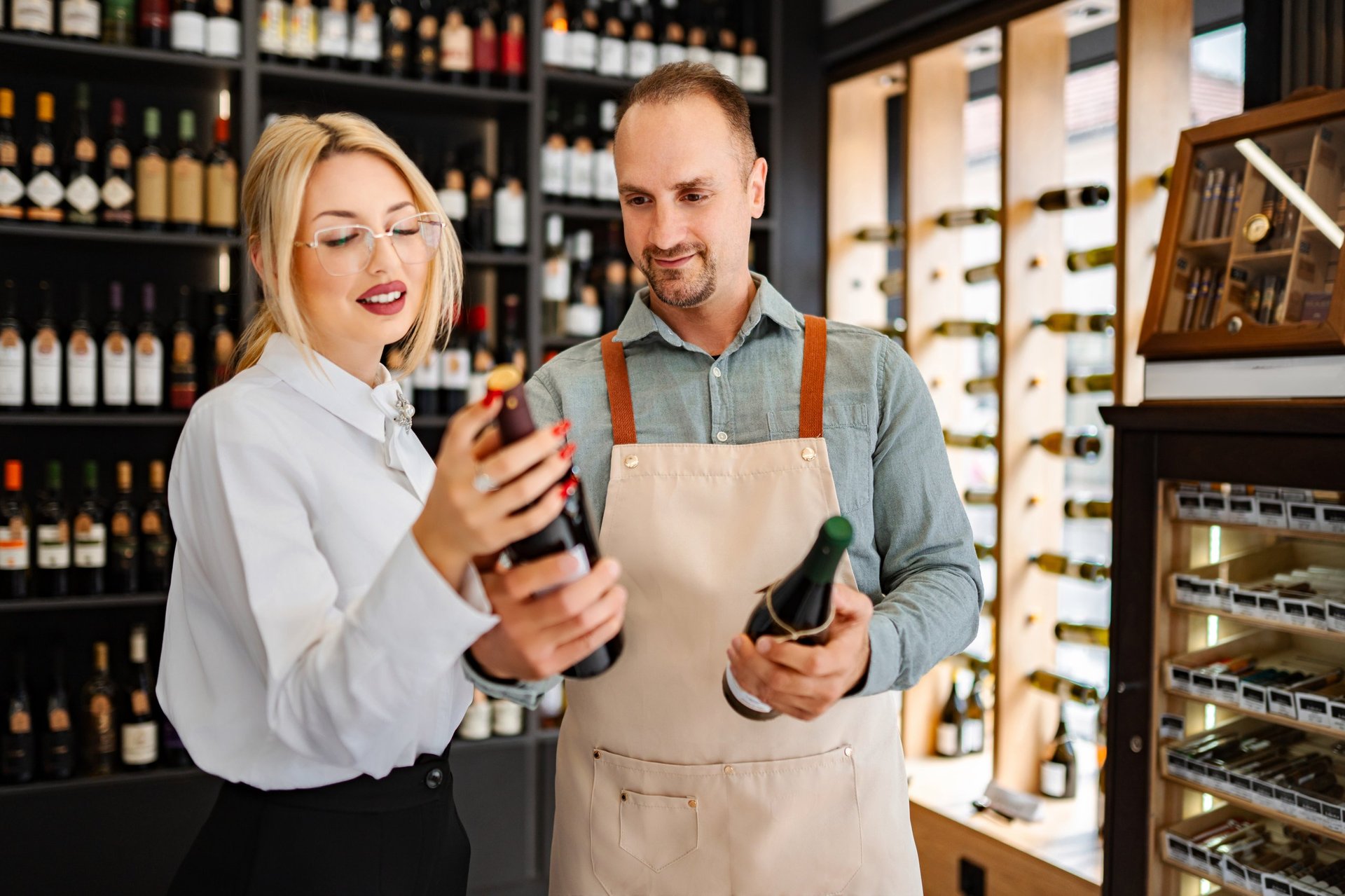Sommelier y cliente seleccionando botellas de vino de un estante en una vinoteca moderna