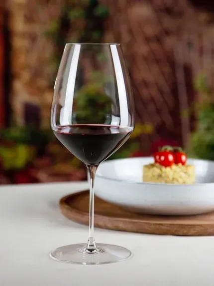 Glass of red wine on white table with plated dessert and blurred garden background