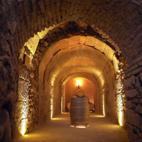 Illuminated stone archway tunnel with wooden barrel inside, warm golden lighting highlighting the curved brick walls